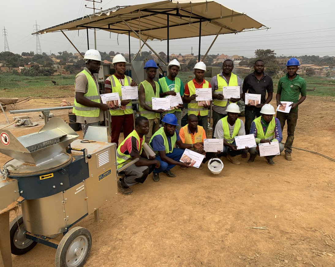 Ici, vous voyez des personnes qui ont reçu un certificat et qui se tiennent devant une machine à blocs de terre comprimée.