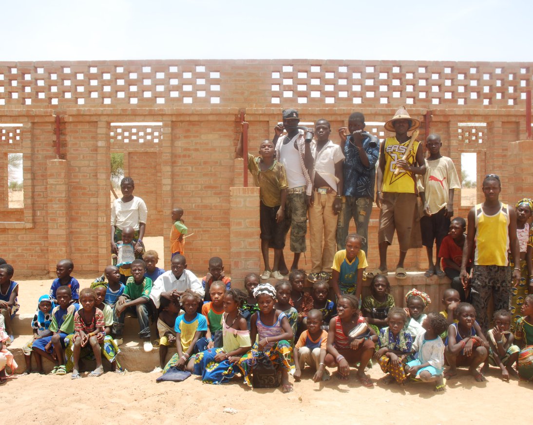 People in front of a compressed earth block building, made of clay bricks.